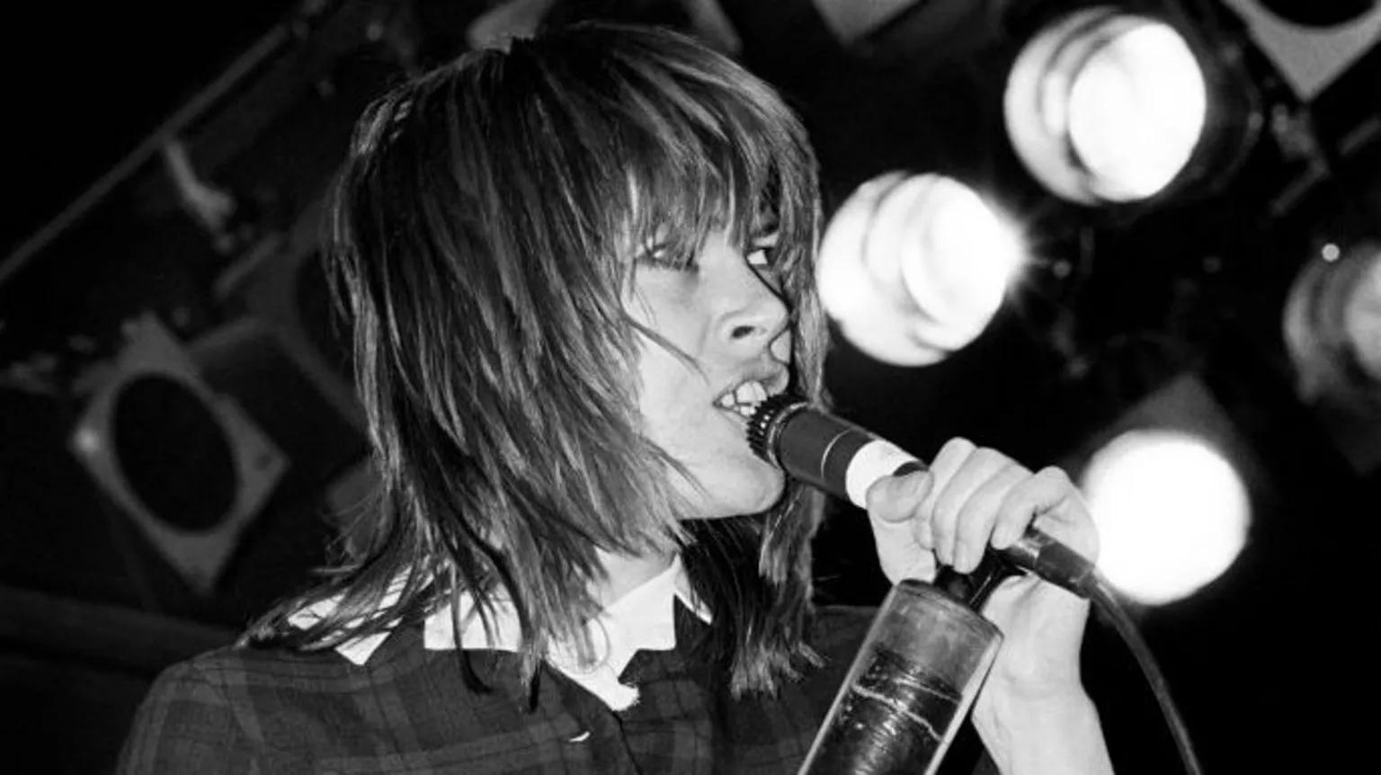 Getty Images Chrissy Amphlett, with shoulder-length hair and a fringe, singing into a microphone with blurred stage lights in background